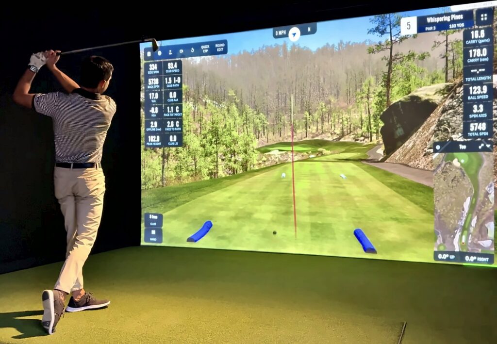 Jay finishing an iron shot in GSPro at Whispering Pines, with the shot data on both sides of the screen, in a Carl's Place PRO enclosure