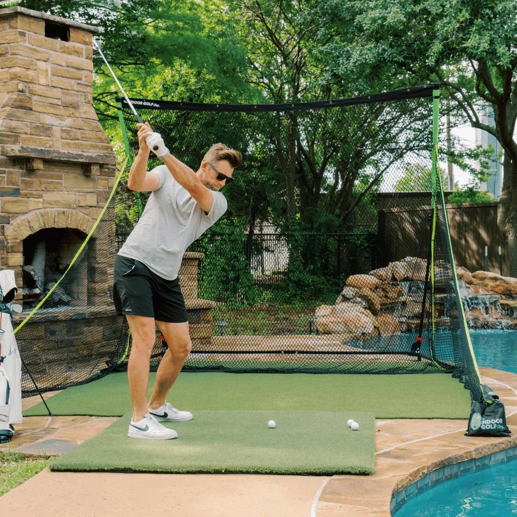 A golfer hitting into the SIGPRO Golf Net from a hitting mat on a patio