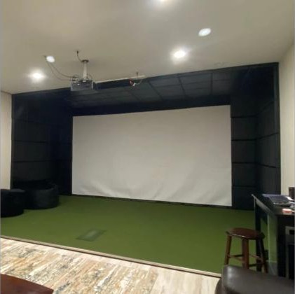 Black SIGPRO wall padding panels on the side walls and ceiling around a white impact screen in a built-in golf simulator room